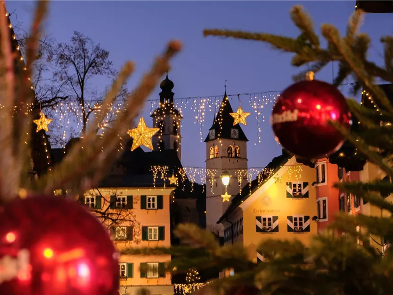 Blick auf beleuchtete Häuserfassaden und Kirchtürme in Kitzbühel mit Weihnachtsdekoration im Vordergrund.