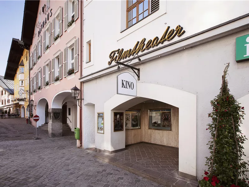 Ein charmantes Kino mit der Aufschrift "KINO" in einem historischen Gebäude. Die Straße ist gepflastert und von bunten Häusern gesäumt.