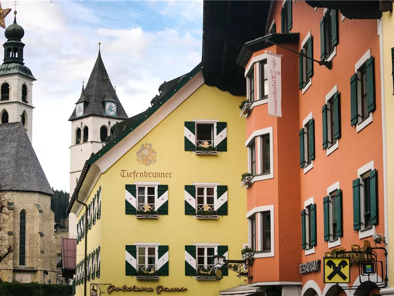 Eine malerische Stadtansicht mit bunten Häusern und einem Kirchturm im Hintergrund. Der Himmel ist leicht bewölkt und verleiht der Szene eine ruhige Atmosphäre.