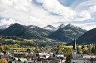 Eine malerische Stadt mit bunten Häusern und einer Kirche im Vordergrund. Im Hintergrund erheben sich majestätische Berge unter einem klaren Himmel.