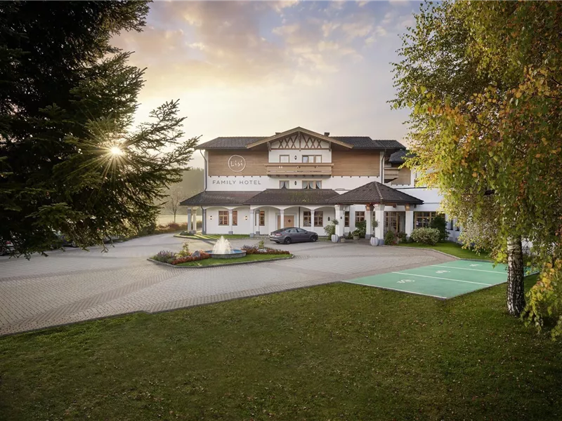 Außenansicht des Lisi Family Hotels mit gepflastertem Vorplatz, Springbrunnen und Bäumen bei Sonnenuntergang.