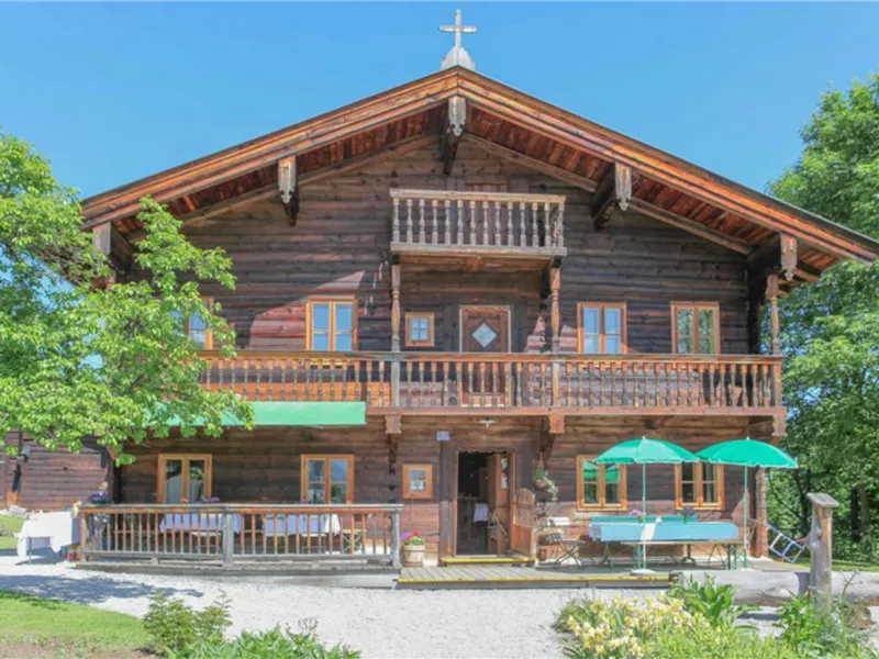 Ein charmantes Holzhaus im alpinen Stil mit einem großen Balkon. Umgeben von Bäumen und einem grünen Garten.