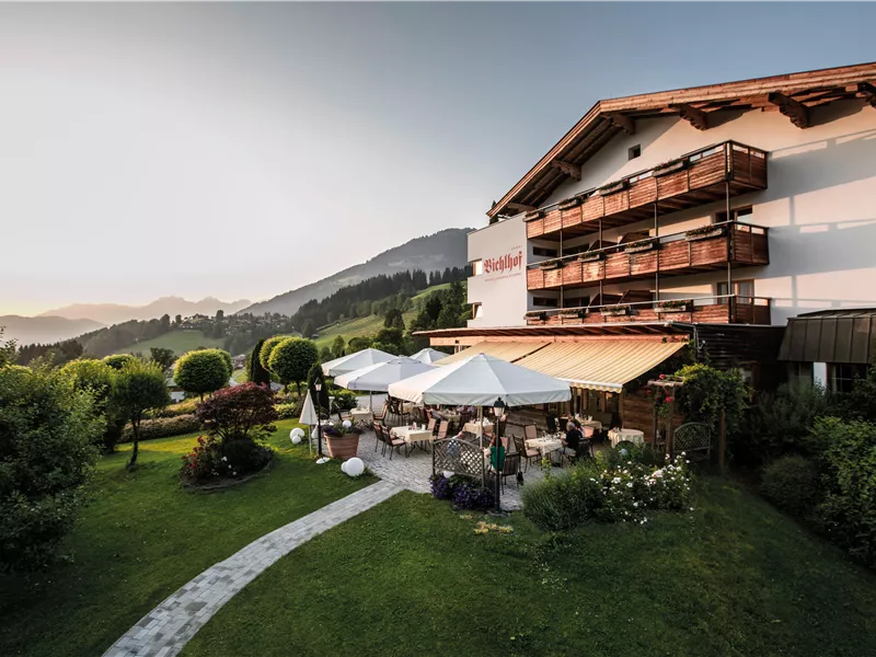 Außenterrasse des Hotels Bichlhof mit Sonnenschirmen und Blick auf die umliegenden Berge bei Sonnenuntergang.