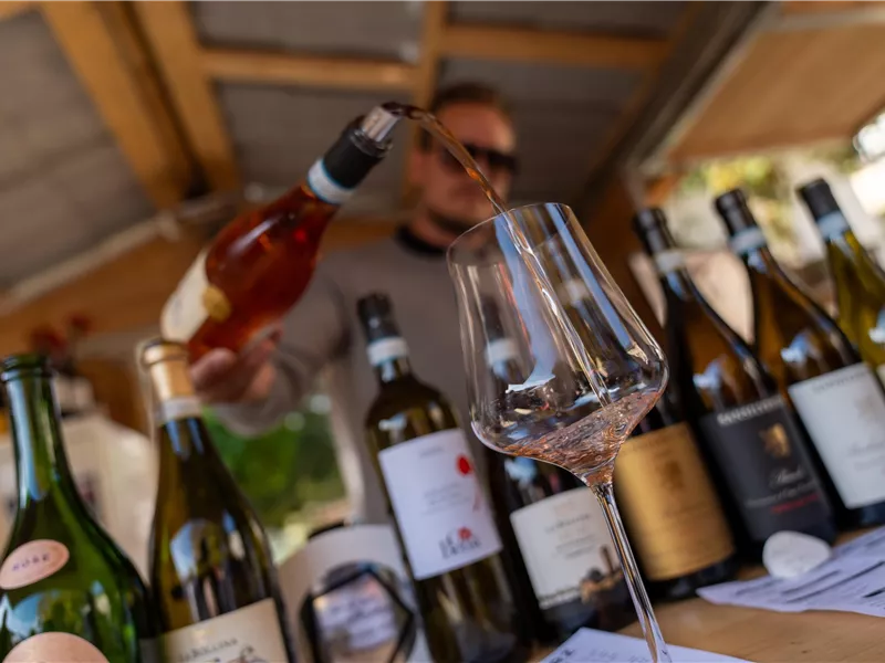Ein Weinfest mit verschiedenen Weinflaschen auf einem Tisch. Eine Person schenkt gerade Roséwein in ein Glas ein.