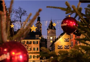 Blick auf beleuchtete Häuserfassaden und Kirchtürme in Kitzbühel mit Weihnachtsdekoration im Vordergrund.