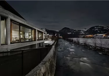 Ein traditionelles bayerisches Ferienhaus umgeben von einer grünen Wiese und Bergen. Es hat Holzbalustraden und Fenster mit Blumenkästen.