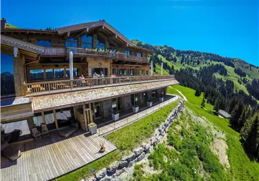 Ein modernes Chalet in den Bergen mit großen Fenstern und einem herrlichen Blick auf die grüne Landschaft. Die sonnige Terrasse lädt zum Entspannen ein.