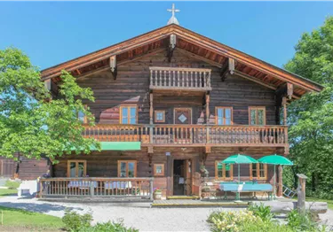 Ein charmantes Holzhaus im alpinen Stil mit einem großen Balkon. Umgeben von Bäumen und einem grünen Garten.
