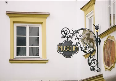 Eine malerische Dorfansicht mit einer Kirche und umliegenden Bergen. Die Landschaft ist grün mit vielen Bäumen und traditionellen Gebäuden.