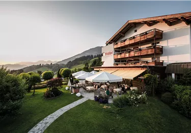 Außenterrasse des Hotels Bichlhof mit Sonnenschirmen und Blick auf die umliegenden Berge bei Sonnenuntergang.