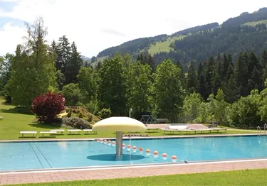 Ein Schwimmbad umgeben von üppigem Grün und Bergen. Die Landschaft ist hell und einladend.