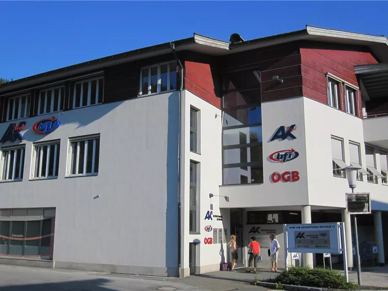 Mehrstöckiges Bürogebäude mit weißer Fassade, roten Akzenten und Logos von AK, bfi und ÖGB.