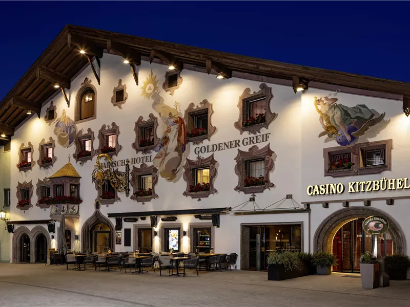 Ein traditionelles Gebäude mit kunstvoll bemalten Fassaden und vielen Fenstern. Das Casino Kitzbühel ist an der Vorderseite deutlich sichtbar.