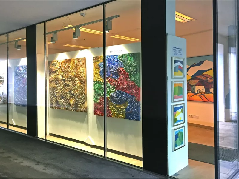 Eine moderne Galerie mit großen, bunten Gemälden an der Wand. Der Eingangsbereich ist hell und einladend gestaltet.