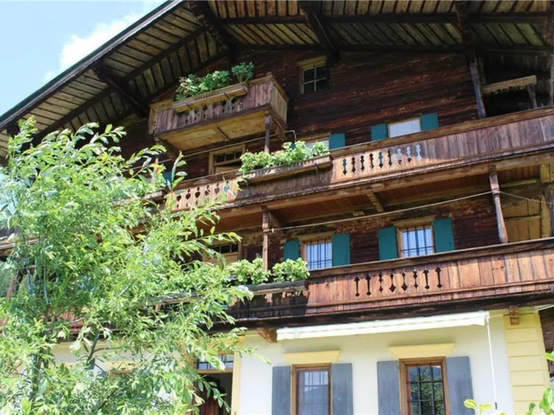 Ein traditionelles Holzhaus mit mehreren Balkonen und grünen Pflanzen. Im Hintergrund ist eine schöne, natürliche Umgebung zu sehen.