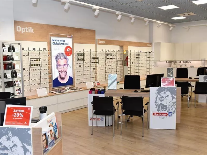 Ein modernes Optikgeschäft mit vielen Brillenmodellen und einem einladenden Empfangsbereich. An der Wand hängen Displays mit aktuellen Angeboten.