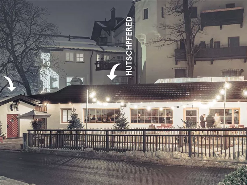 Ein gemütliches Restaurant im Winter, beleuchtet mit warmen Lichtern. Schnee liegt auf dem Boden und die Umgebung wirkt ruhig und einladend.