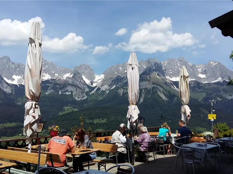 Ein gemütliches Café mit Blick auf majestätische Berge. Die Gäste sitzen draußen unter Sonnenschirmen und genießen die Aussicht.