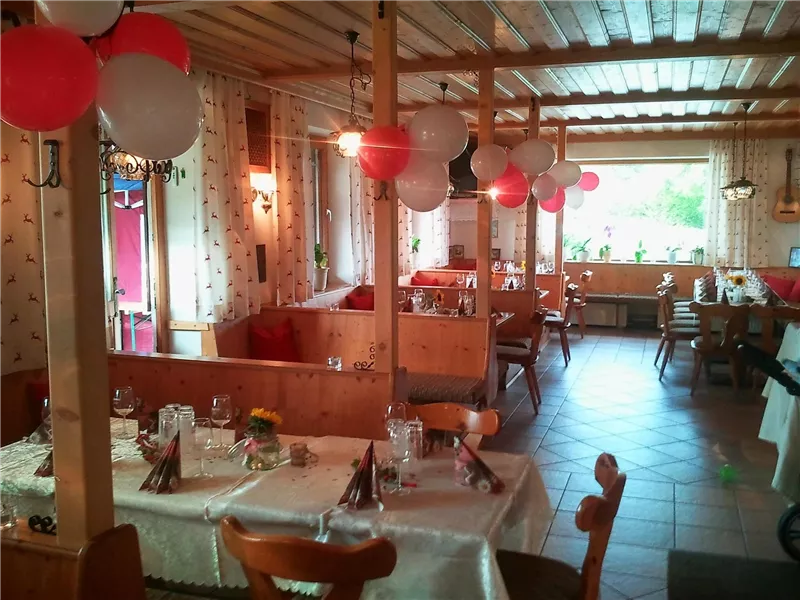 Ein gemütliches Restaurant mit Holzdekor und festlicher Dekoration. Rote und weiße Ballons hängen von der Decke, während die Tische für Gäste vorbereitet sind.