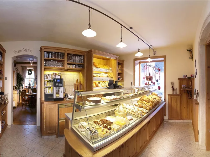 Ein gemütliches Café mit einer Theke voller Kuchen und Gebäck. Helle Holzmöbel und ein einladendes Ambiente schaffen eine warme Atmosphäre.