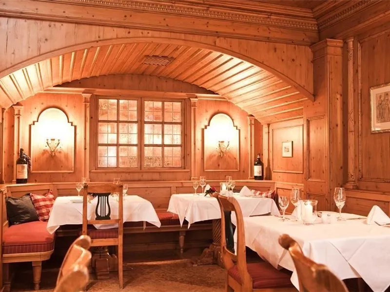 Ein gemütliches Restaurant mit Holzverkleidung und warmem Licht. Es sind elegante Tischdecken und Weingläser auf den Tischen gedeckt.