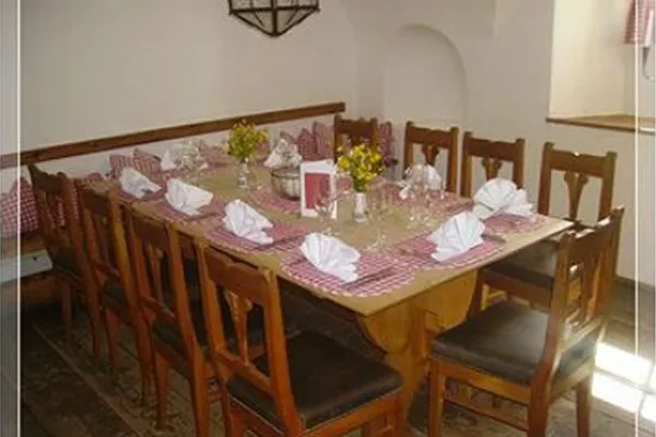 Ein festlich gedeckter Tisch in einem gemütlichen Raum. Die Stühle sind aus Holz und die Tischdeko besteht aus Blumen und Stoffservietten.