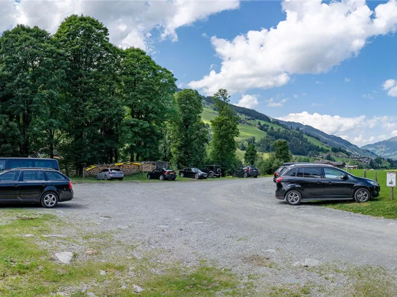Ein Parkplatz umgeben von grünen Bäumen und Hügeln. Der Himmel ist blau mit einigen weißen Wolken.
