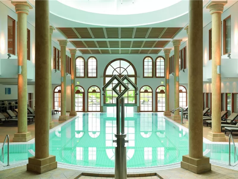 Ein eleganter Poolbereich mit großen Fenstern und Säulen. Das Wasser ist klar und die Atmosphäre ist entspannend.