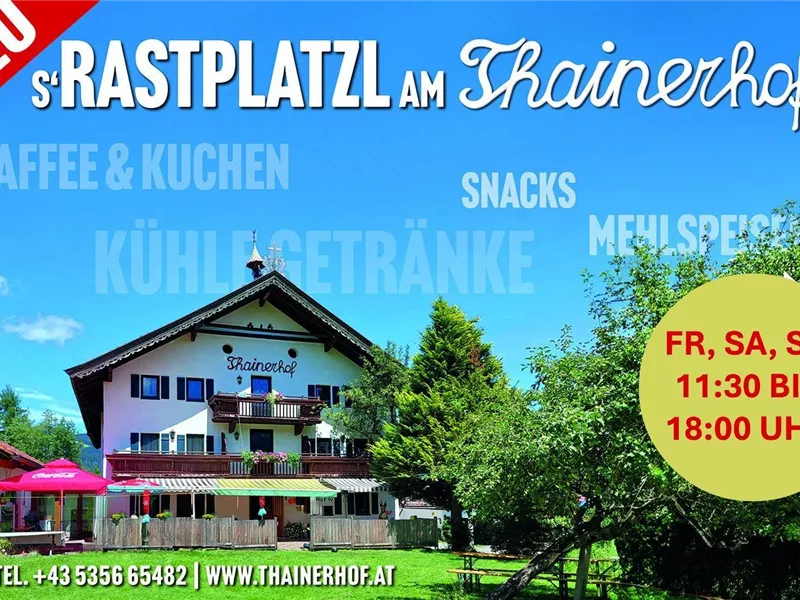 Außenansicht des Thainerhofs mit Terrasse, Sonnenschirmen und umliegenden Bäumen unter blauem Himmel.