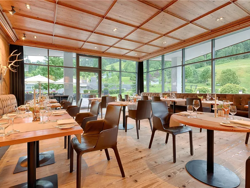 Ein modernes Restaurant mit großen Fenstern und Blick auf die grünen Hügel. Die Einrichtung ist stilvoll mit Holzmöbeln und eleganten Tischgedecken.