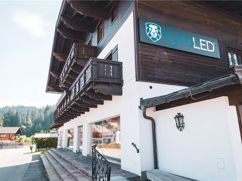 Ein modernes Geschäftshaus mit Holzverkleidung und einem Schild, das "Lite LED" zeigt. Die Umgebung ist ländlich mit Bäumen im Hintergrund.