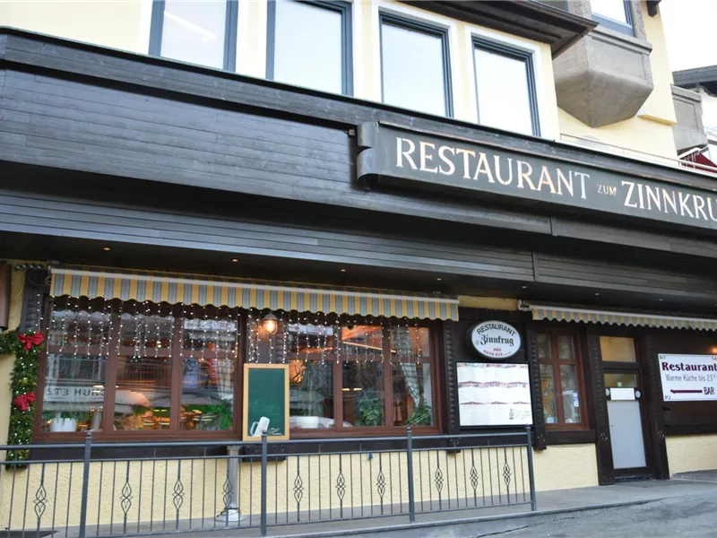 Ein gemütliches Restaurant mit der Aufschrift "Zinnkrug". Die Fassade ist stilvoll gestaltet und mit Pflanzen dekoriert.