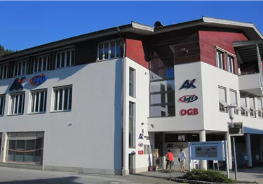 Mehrstöckiges Bürogebäude mit weißer Fassade, roten Akzenten und Logos von AK, bfi und ÖGB.