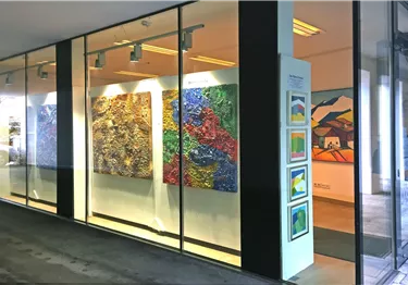Eine moderne Galerie mit großen, bunten Gemälden an der Wand. Der Eingangsbereich ist hell und einladend gestaltet.