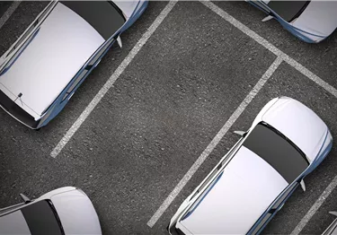 Ein Parkplatz mit mehreren weißen Autos, die ordentlich in den Stellplätzen stehen. Die Fläche ist aus grauem Asphalt.