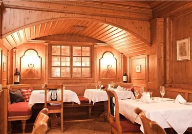 Ein gemütliches Restaurant mit Holzverkleidung und warmem Licht. Es sind elegante Tischdecken und Weingläser auf den Tischen gedeckt.