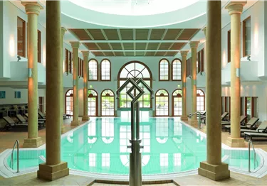 Ein eleganter Poolbereich mit großen Fenstern und Säulen. Das Wasser ist klar und die Atmosphäre ist entspannend.