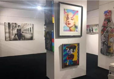 Eine Kunstgalerie mit mehreren Rahmen und bunten Gemälden. Die Wände sind mit verschiedenen Kunstwerken dekoriert, darunter ein Porträt und eine Fotografie.